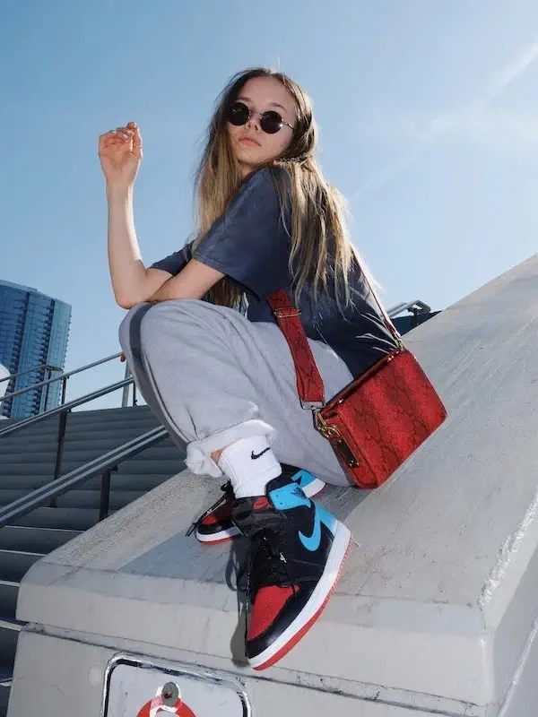 woman posing on concrete block with sunglasses, a purse, and stylish shoes