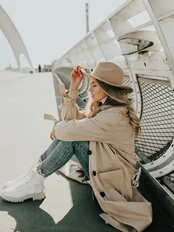 woman sitting in a trench coat and distressed jeans wearing a hat